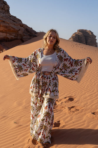A Woman in a boho floral outfit standing in a desert landscape with sand dunes and rock formations.
