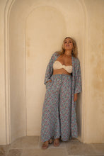 A Woman wearing a boho floral outfit standing against a beige wall.