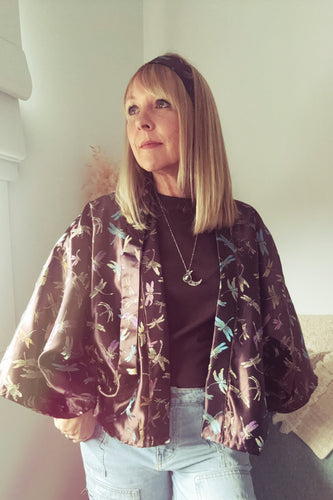 A Woman wearing a boho floral jacket over a dark top and light jeans indoors.