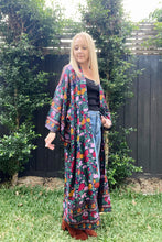 Woman wearing a colorful floral boho  kimono in an outdoor setting with greenery.